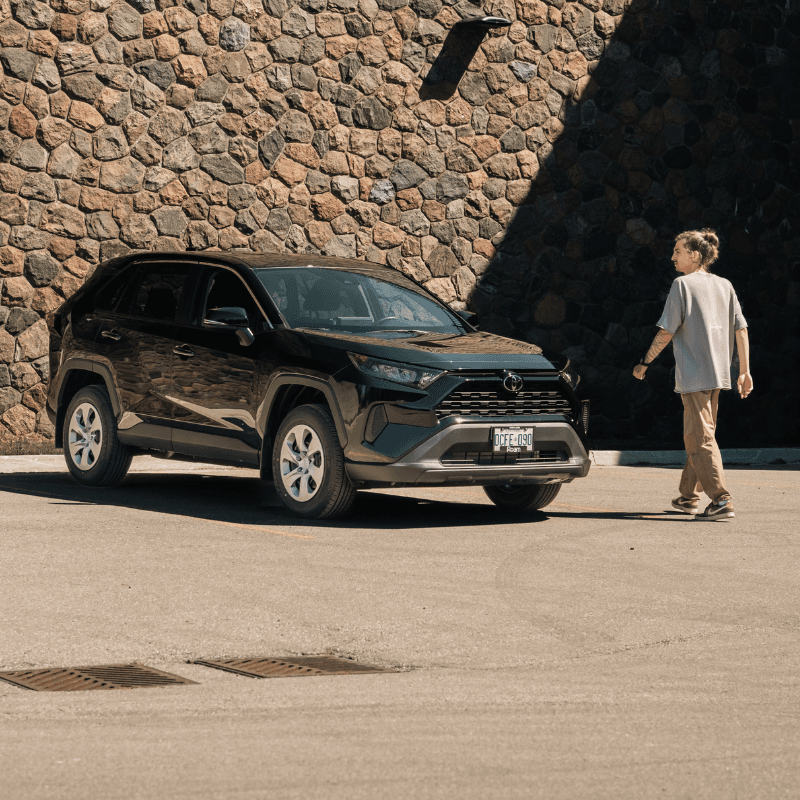 Man walking towards a dark SUV on a sunny day