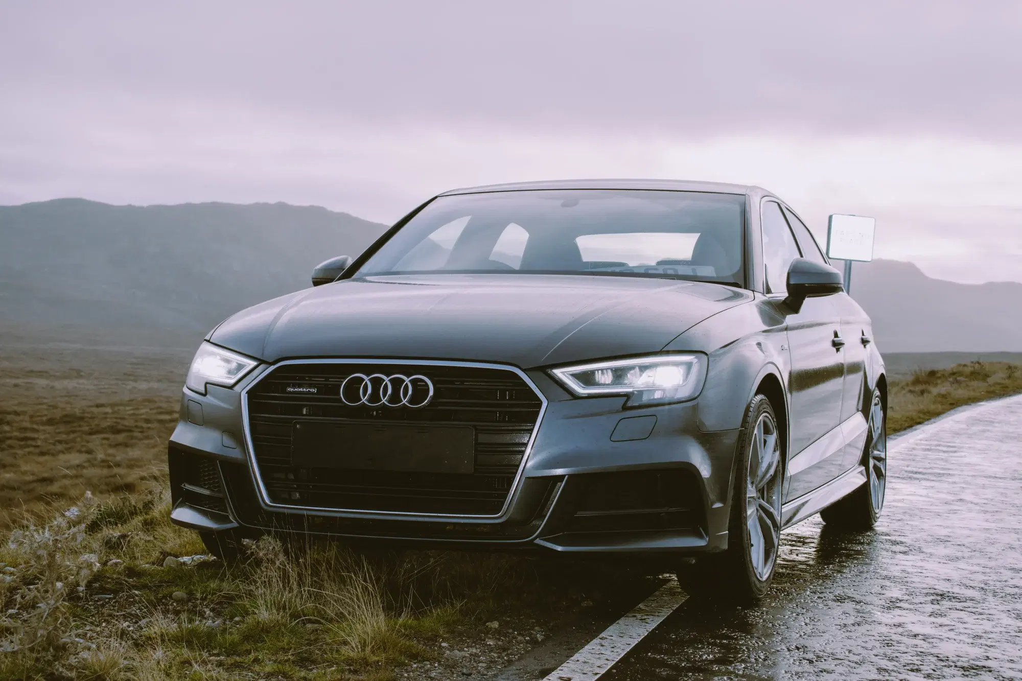 Grey Audi sedan on a wet coastal road with misty hills in the background