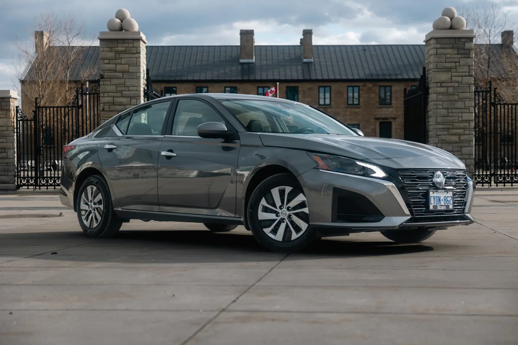 Metallic grey Nissan Altima sedan parked in front of a historic stone building with a wrought-iron gate