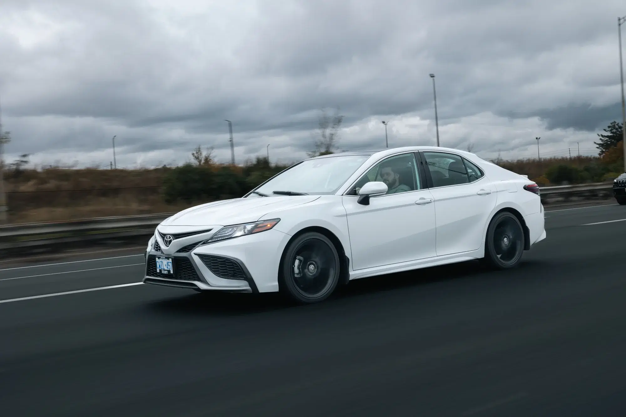 White Toyota Camry sedan on a highway under an overcast sky